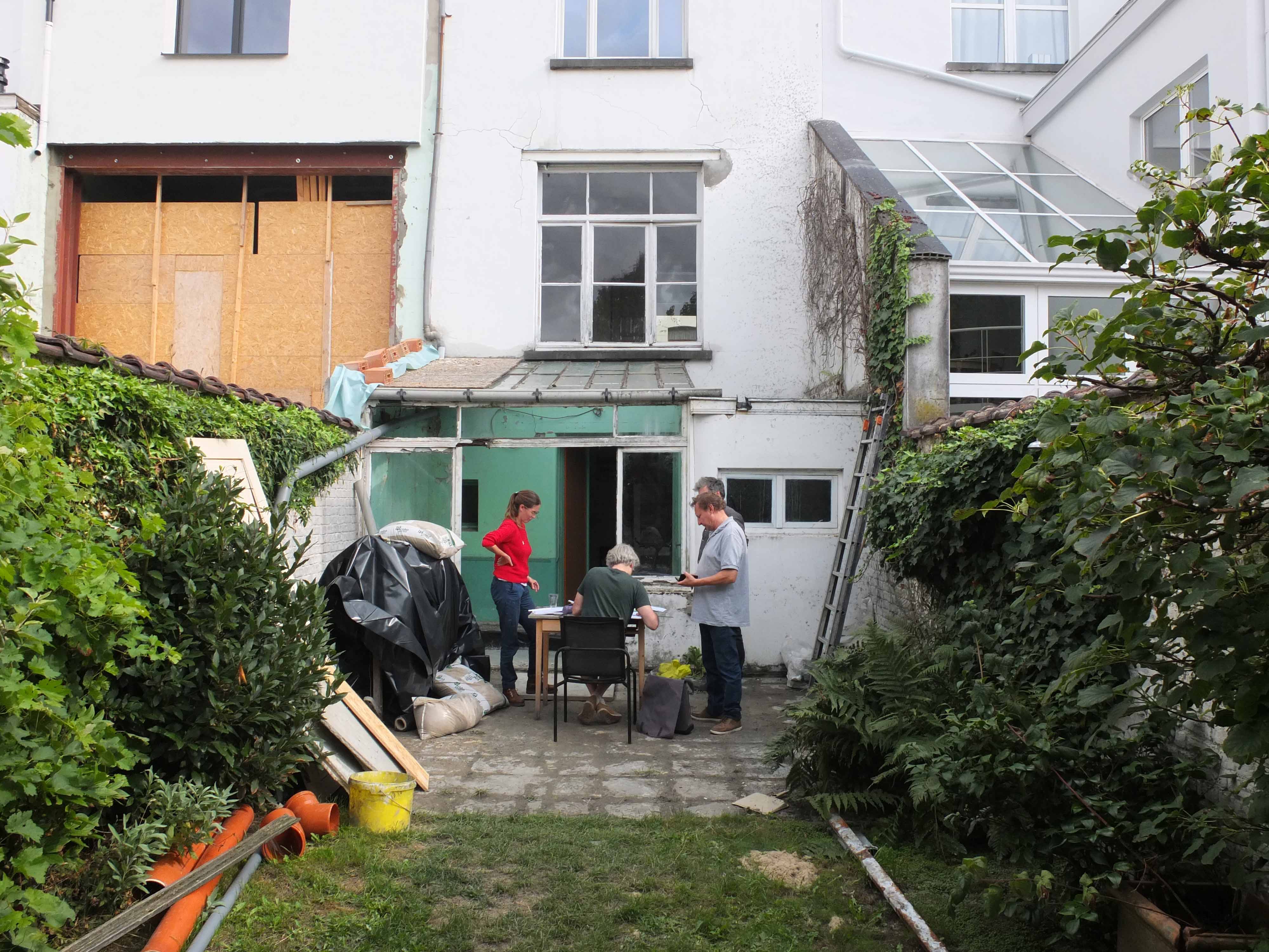 photo de chantier en cours : depuis le jardin, vue sur la façade arrière et l'équipe architecte, maître d'ouvrage et ingénieur en plein discussion autour d'une table